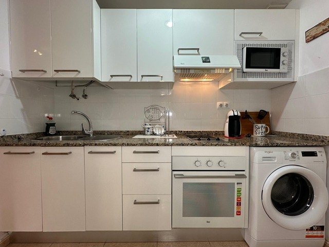 Galley kitchen with white units, granite worktops, oven, hob, microwave and washing machine